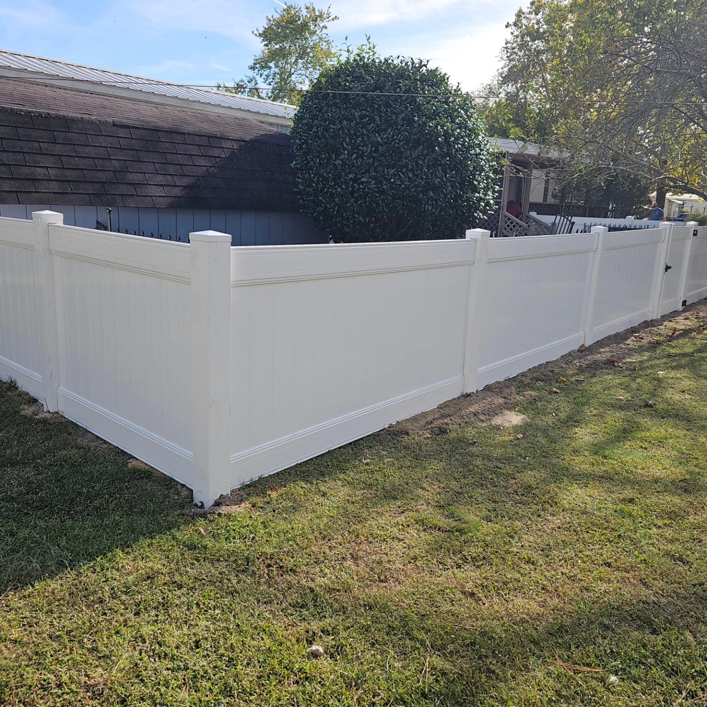 White vinyl privacy fence installed around a backyard lawn