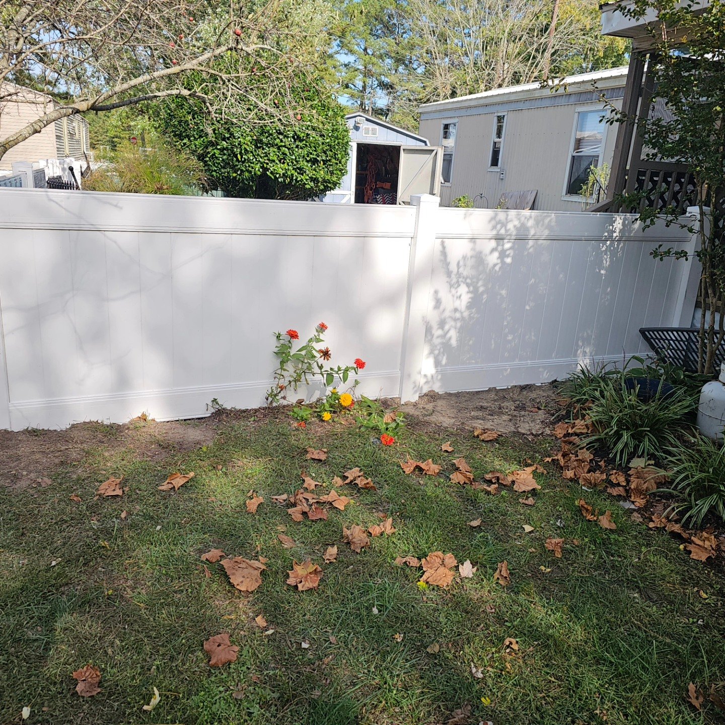 White vinyl fence installation with fall leaves on the lawn